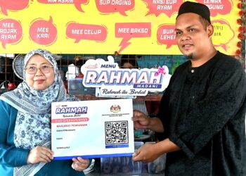 FUZIAH Salleh menyerahkan replika 'Kad Diskaun Khas' Menu Rahmah kepada Wan Ahmad Hafidzul Wan Sulong, 39, di gerainya di Pekan, Pahang. - FOTO/SHAIKH AHMAD RAZIF