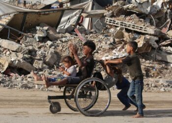 KANAK-KANAK Palestin menolak rakan mereka atas kerusi roda melalui runtuhan bangunan di tengah Gaza. - AFP