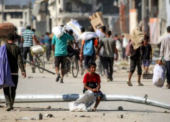 SEORANG budak lelaki duduk di atas tiang lampu yang tumbang ketika orang ramai mengambil bantuan kemanusiaan di koridor Netzarim, di Nuseirat, tengah Gaza.- AFP
