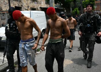 PEGAWAI polis mengiringi suspek yang ditahan dalam operasi membanteras dadah di kawasan setinggan Vila Cruzeiro di Rio de Janeiro, Brazil.-AFP