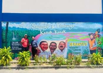 Marhaizan Mahayudin (kiri) bersama seorang guru di samping catan dinding bertemakan Sayangi Kanak-kanak, program advokasi sebuah agensi kerajaan sebuah sekolah menengah di Jerantut, Pahang.