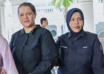 TERTUDUH (kiri) diiringi oleh seorang anggota polis ketika dihadapkan ke Mahkamah Majistret George Town, Pulau Pinang hari ini atas pertuduhan mengugut untuk menyebarkan gambar bogel seorang kenalan lelaki, Jun lalu.-UTUSAN/DANIAL SAAD