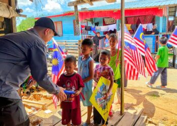 Mejar Mohd. Zurul Kamal menyantuni anak-anak  Kampung  Sungai Melayu di Pulau Sebatik, Sabah dengan  memasang bendera Malaysia bersama-sama.