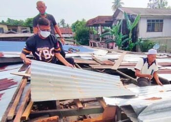 Hanafiah Mat (tengah) tidak kekok membantu membaik pulih bumbung rumah penduduk yang rosak di Chukai, baru-baru ini.