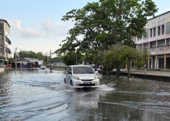 KENDERAAN melalui jalan yang dinaiki air pasang besar di bandar Teluk Intan hari ini. - UTUSAN/AIN SAFRE BIDIN