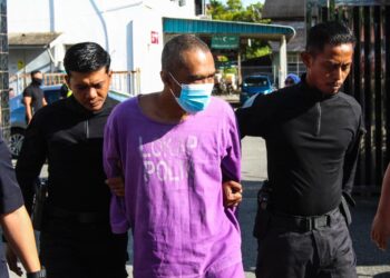 TERTUDUH diiringi polis semasa menghadiri prosiding di perbicaraan di Mahkamah Tumpat, Kelantan. - UTUSAN/KAMARUL BISMI KAMARUZAMAN