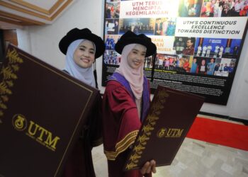 Pasangan adik-beradik, Nor Athirah Zaharudin (kiri) Nur Zafirah Zaharudin bangga menerima PhD pada Majlis Konvokesyen Ke-69 UTM, Skudai, Johor Bahru, hari ini. - UTUSAN/RAJA JAAFAR ALI