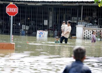 SEORANG penduduk meredah banjir sambil mendukung anaknya berikutan ban pecah di pintu air utama Sungai Skudai di Kampung Pasir, Tampoi, Johor Bahru. - UTUSAN/RAJA JAAFAR ALI