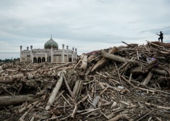 SEORANG lelaki merakam gambar sebuah sekolah pondok yang terjejas akibat banjir besar dari atas timbunan kayu balak di Aceh Tamiang, Sumatera Utara. - AFP