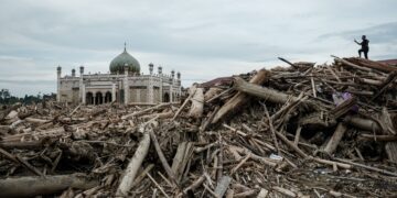 SEORANG lelaki merakam gambar sebuah sekolah pondok yang terjejas akibat banjir besar dari atas timbunan kayu balak di Aceh Tamiang, Sumatera Utara. - AFP