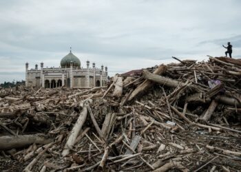 SEORANG lelaki merakam gambar sebuah sekolah pondok yang terjejas akibat banjir besar dari atas timbunan kayu balak di Aceh Tamiang, Sumatera Utara. - AFP