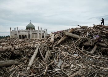 SEORANG lelaki merakam gambar sebuah sekolah pondok yang terjejas akibat banjir besar dari atas timbunan kayu balak di Aceh Tamiang, Sumatera Utara. - AFP