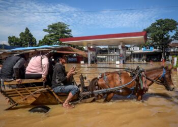 SEBUAH kereta kuda membawa penumpang merentasi jalan yang dinaiki air banjir berhampiran sebuah stesen minyak terbiar di Bandung, Jawa Barat. – AFP