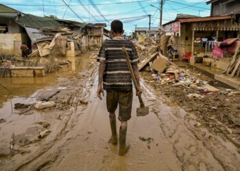 SEORANG lelaki berjalan sambil membawa cangkul di jalan yang dipenuhi lumpur tebal akibat banjir besar di Aceh Tamiang, wilayah Aceh. - AFP