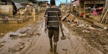 SEORANG lelaki berjalan sambil membawa cangkul di jalan yang dipenuhi lumpur tebal akibat banjir besar di Aceh Tamiang, wilayah Aceh. - AFP
