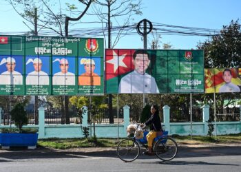 SEORANG wanita menunggang basikal melalui papan iklan memaparkan calon kempen pilihan raya di Mandalay, Myanmar. – AFP
