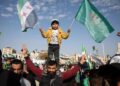 KANAK-kanak Syria memegang bendera negara sambil berdiri di atas bahu seorang lelaki semasa sambutan setahun serangan Islamis menumbangkan pemerintah lama di Hama, Syria.- AFP