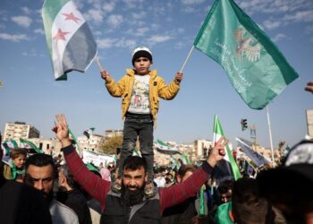 KANAK-kanak Syria memegang bendera negara sambil berdiri di atas bahu seorang lelaki semasa sambutan setahun serangan Islamis menumbangkan pemerintah lama di Hama, Syria.- AFP