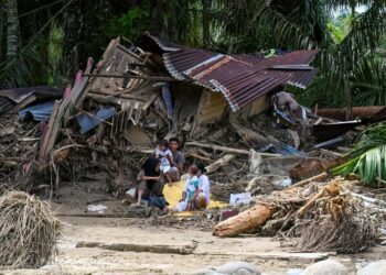 PENDUDUK kampung duduk di luar rumah mereka yang rosak akibat banjir kilat di Garoga, wilayah Sumatera Utara.- AFP