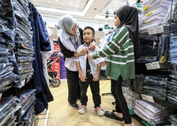 SITI Aznur Mohd Salleh mencuba pakaian sekolah kepada anaknya, Asyraf Shiraz Aznee Hanafis sebagai persiapan menjelang pembukaan sesi persekolahan 2026 ketika tinjauan di sebuah pusat beli belah di ibu kota semalam. – UTUSAN/FARIZ RUSADIO