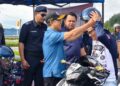 JOACHIM Gunsalam (dua dari kiri) membantu seorang penunggang motosikal memakai topi keledar semasa kempen keselamatan jalan raya di Kundasang. - IHSAN MEDIA KKRU