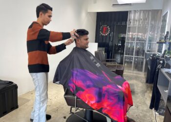 Muhammad Afiq Afifi Mohammad Sufri tekun menggayakan rambut pelanggan.
