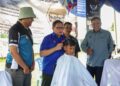 MUHD. Khair Razman Mohamed Annuar memotong rambut seorang pelajar sempena Majlis Kenduri Rakyat Desa MADANI 2025 pada 
program Kampung Angkat Madani dan Sekolah Angkat MADANI di padang SK Bukit Sapi, di Lenggong kelmarin. – UTUSAN/MUHAMAD NAZREEN SYAH MUSTHAFA