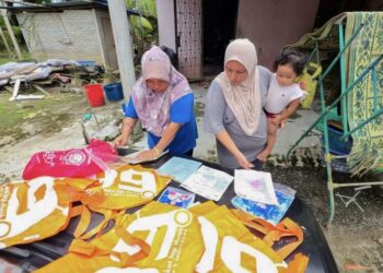FAUZIAH Johari bersama anak dan cucunya menjemur buku sekolah dan dokumen lain yang rosak akibat banjir di rumah mereka Kampung Glouster di Jalan Changkat Jong, Teluk Intan, Perak, semalam. - UTUSAN/AIN SAFRE BIDIN