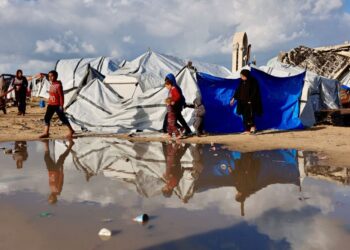 PENDUDUK Palestin berjalan melepasi lopak air berhampiran khemah perlindungan ketika kawasan itu mengalami hujan dan cuaca sejuk di Gaza City.-AFP