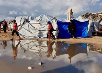 PENDUDUK Palestin berjalan melepasi lopak air berhampiran khemah perlindungan ketika kawasan itu mengalami hujan dan cuaca sejuk di Gaza City.-AFP