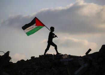 SEORANG kanak-kanak Palestin mengibarkan bendera kebangsaan ketika berjalan di atas runtuhan bangunan di kem Bureij, di tengah Gaza.- AFP