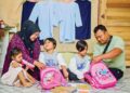 MOHD. Taufiq Mat Rohek dan Nurul Wathiqah Ab. Wahab  melayan anak kembar mereka mengemas kelengkapan persekolahan sebagai persediaan sesi persekolahan baharu semalam di Kampung Wakaf Tapai, Marang, Terengganu. – UTUSAN/PUQTRA HAIRRY