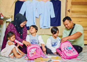 MOHD. Taufiq Mat Rohek dan Nurul Wathiqah Ab. Wahab  melayan anak kembar mereka mengemas kelengkapan persekolahan sebagai persediaan sesi persekolahan baharu semalam di Kampung Wakaf Tapai, Marang, Terengganu. – UTUSAN/PUQTRA HAIRRY