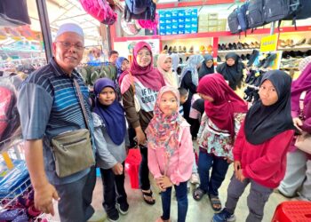 IBRAHIM Arshad bersama murid yang membeli pakaian sekolah di sebuah kedai di Teluk Intan, Perak, semalam. – UTUSAN/AIN SAFRE BIDIN