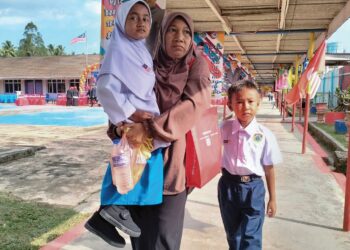 SITI Nor Najwa Zulkifli didukung ibunya pada hari pertama sesi persekolahan di Sekolah Menegah Kebangaaan (SMK) Pulau Beluru Sekolah Model Khas Komprehensif 11 (K11) di Pulau Beluru Tumpat, Kelantan. – UTUSAN/ROHANA ISMAIL