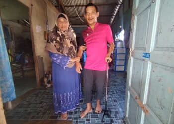 MOHAMAD Najmi Daud dipapah ibunya di rumah mereka di Kampung Tengah, Kuala Besut, Terengganu. – UTUSAN/WAN ZURATIKAH IFFAH WAN ZULKIFLI