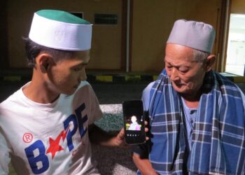 MOHD. Shahril (kiri) dan Mat Jusoh menunjukkan gambar arwah Nik Azmi ketika ditemui di pekarangan Unit Forensik Hospital Gua Musang, Gua Musang hari ini.