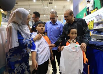 NIZAM Sani (tengah) dan Pengarah Eksekutif Mydin, Ahimmat Mydin (kanan) ketika mencuba pakaian kepada pelajar pada Majlis Penyerahan Inisiatif Jangkauan Komuniti Madani Kembali ke Sekolah 2026 di Mydin Subang Jaya di sini, semalam. - UTUSAN/ISKANDAR ISHAK