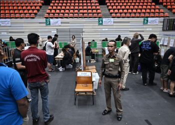 POLIS memantau orang ramai membuang undi semasa pengundian awal di Bangkok, menjelang pilihan raya umum 8 Februari.- AFP
