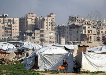 SEORANG lelaki duduk di luar khemah berhampiran bangunan yang rosak di kem pelarian Maghazi untuk pelarian Palestin, tengah Gaza. - AFP