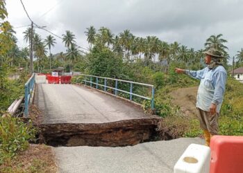 CHE Rahim Che Harun menunjukkan jambatan yang putus dan ditutup sepenuhnya di Kampung Pandu di Batu Rakit, Kuala Nerus, Terengganu. – UTUSAN/ ERMA YUSNIDA JUSOH