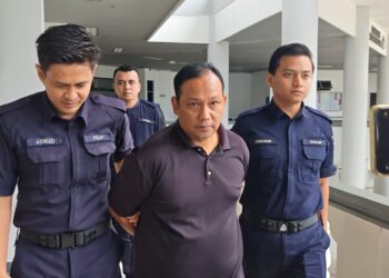 TERTUDUH diiringi anggota polis keluar dari Mahkamah Majistret Ayer Keroh selepas dijatuhi hukuman denda RM6,000 kerana menyamar sebagai anggota polis dan memeras ugut warga asing.-UTUSAN/AMRAN ALI.