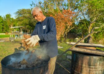 AHMAD Osman memproses dan membakar tempurung kelapa untuk dijadikan arang bagi memenuhi tempahan para peniaga bazar Ramadan di Perlis.– UTUSAN/IZLIZAN OTHMAN