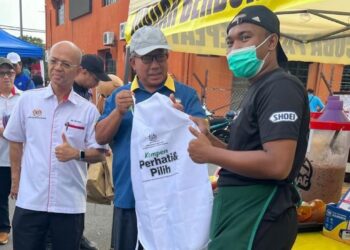 MEGAT Hashirat Hassan (tengah) dan Ghazali Chik (kiri) menyerahkan apron kepada peniaga bazar Ramadan sempena Program Kick-Off Keselamatan Makanan di Bazar Ramadan Arau, Perlis, semalam. - UTUSAN/ASYRAF MUHAMMAD