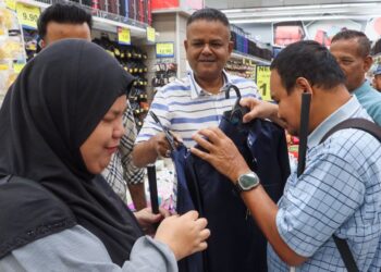 KADHAR Shah Abdul Razak (tengah) membantu Nur Layli Adi Mesra (kiri) dan Mohd. Hakimi Mohd. Zainol (kanan) memilih baju raya yang sesuai di sebuah pasar raya di Bukit Mertajam, Pulau Pinang, petang semalam.-UTUSAN/DANIAL SAAD