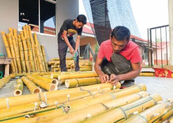 MOHAMAD Helmie Shafie (kiri) dan Sayful Amir Samsudin tekun menyiapkan tempahan pelita buluh kuning di Changlun, Kubang Pasu.