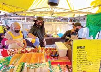 NORHISHAM Ashar (tengah) bersama isterinya, Siti Rohayu Md Saad (kiri) dan pekerja mereka menyiapkan pesanan di gerai burger dekat Taman Sophia, Alor Setar, Kedah semalam.