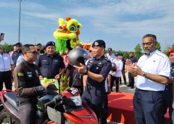 MOHAMMAD Azlin Sadari memakaikan topi keledar kepada penunggang motosikal sambil diperhatikan Lyndon Alfred (kanan) Sempena Kempen Op Selamat sempena Sambutan Tahun Baharu Cina Negeri Perak di Plaza Tol Teluk Intan hari ini.