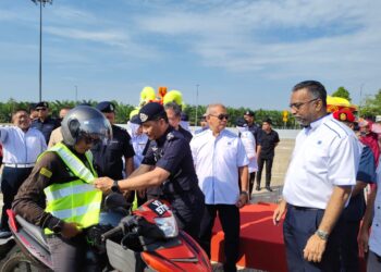 MOHAMMAD Azlin Sadari memakaikan jaket keselamatan kepada penunggang motosikal semasa Kempen Op Selamat sempena Sambutan Tahun Baharu Cina Negeri Perak di Plaza Tol Teluk Intan hari ini.
