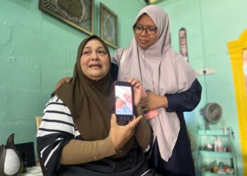 NORHASLINDA Mohd Jusoh (kiri) menunjukkan gambar bersama arwah suami di kediamannya di RPA Padang Besar, Perlis semalam. -UTUSAN/ASYRAF MUHAMMAD